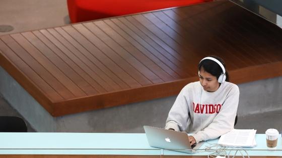 student wearing a 桃瘾社区 sweatshirt and headphones works on a laptop in a modern academic building