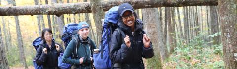 Three students backpacking in the woods walk in a line