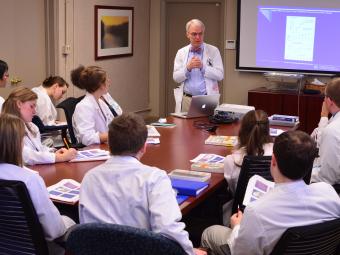 Students gather around a table at Carolinas Medical Center, listening to a lecture while they have a shadowing experience