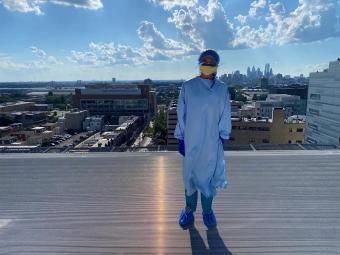 Lilly Sirover 鈥�24 wearing medical scrubs standing on a rooftop platform overlooking many buildings